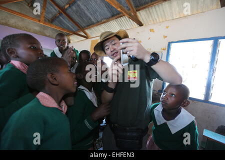 Nairobi, in Kenya. Undicesimo Mar, 2015. Simba (C) mostra una foto sul suo telefono cellulare per i bambini del Kenya in una scuola primaria in Ol Kinyei Conservancy, Kenya, il 11 marzo 2015. Simba, un 43-anno-vecchio uomo cinese, è anche chiamato Zhuo Qiang. Egli fondò Mara Fondo di conservazione, una organizzazione non governativa dedicata alla protezione di leoni e altri animali così come risparmiare il loro habitat naturale nel 2011. Nel corso degli anni, Simba e la sua fondazione sono state offrendo aiutando le mani per la conservancy nonché il Maasai locale di persone nel tentativo di salvare la vita selvaggia. © Pan Siwei/Xinhua/Alamy Live News Foto Stock