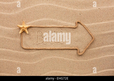 Freccia fatta di corda e conchiglie di mare con la parola Bali sulla sabbia, come sfondo Foto Stock