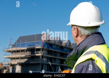 Imprenditore edile, con il suo ritorno alla telecamera, guardando verso un edificio che è coperta da impalcature. Foto Stock