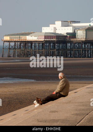 Un uomo seduto sulla riva fasi di Blackpool, guardando fuori verso il molo nord in una giornata di sole. Foto Stock