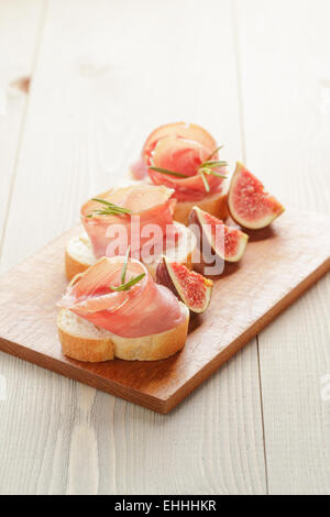 Crostini con prosciutto e fichi sul pannello di legno Foto Stock