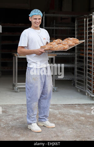 Baker tenendo un vassoio di pane appena sfornato Foto Stock