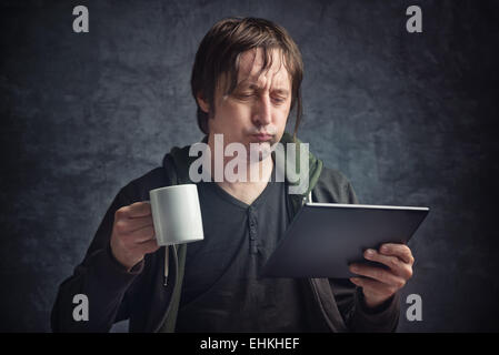 Adulto Uomo caucasico la lettura di cattive notizie sulla tavoletta digitale del computer e del dispositivo di bere il caffè Foto Stock