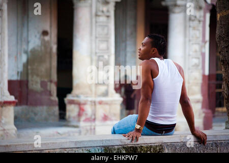 Un giovane uomo si siede sulla strada a l'Avana, Cuba Foto Stock