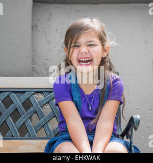 Bambina si siede ridere sul banco all'esterno. Foto Stock