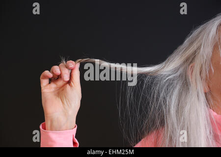 Un senior donna tenendo fuori un filamento dei suoi capelli grigi. Foto Stock