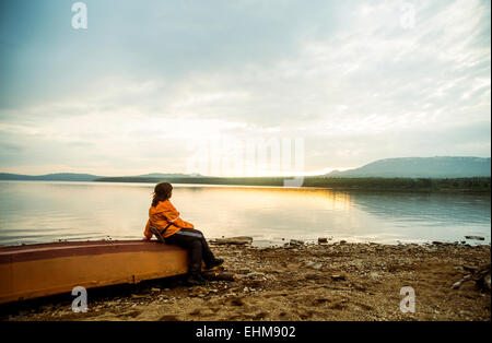 Caucasian donna seduta su fatiscente barca al lago rurale Foto Stock