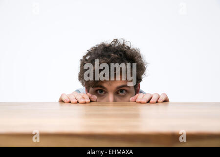 Giovane uomo con capelli ricci spiata da dietro la scrivania Foto Stock