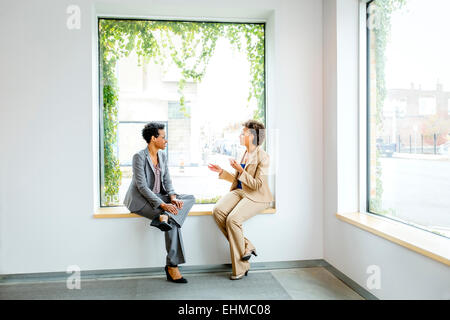 Imprenditrici parlando nella finestra di office lobby Foto Stock