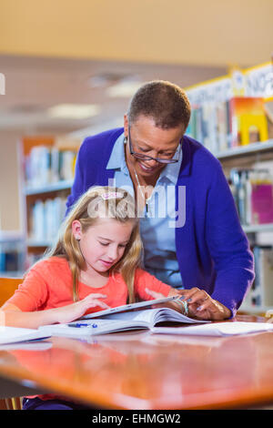 Insegnante aiutando studente usa tavoletta digitale in libreria Foto Stock