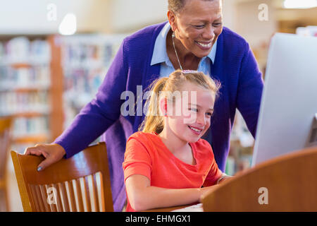 Docente aiutare studenti usano computer in biblioteca Foto Stock