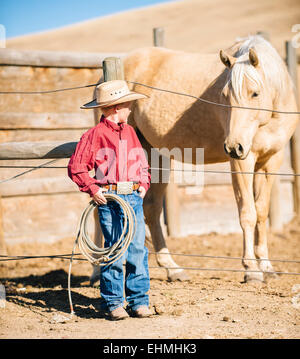 Ragazzo caucasica nel vestito da cowboy ammirando cavalli sul ranch Foto Stock