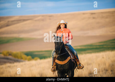 La donna caucasica di equitazione in campo erboso Foto Stock