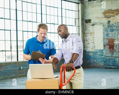 Imprenditori utilizzando laptop in scatole di cartone in magazzino Foto Stock