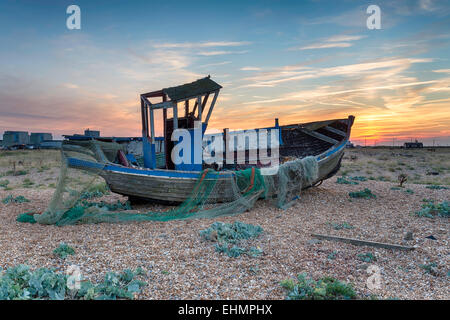 Bellissimo Tramonto spettacolare su un vecchio weathered barca da pesca con reti su una spiaggia ghiaiosa Foto Stock