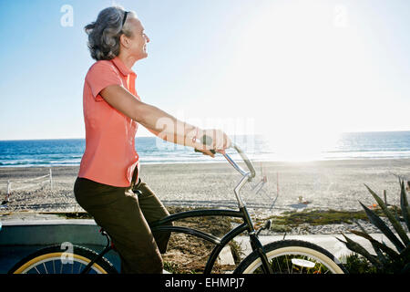 La donna caucasica bicicletta equitazione nei pressi della spiaggia Foto Stock