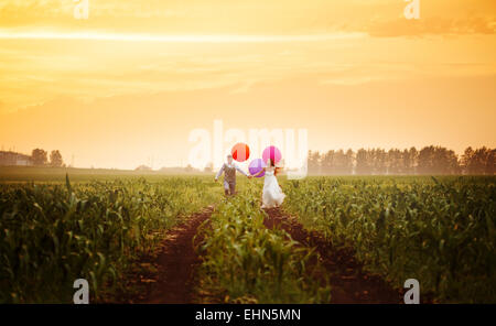 Felice giovani sposi in esecuzione sul campo al tramonto con grande e luminosa palloncini colorati Foto Stock