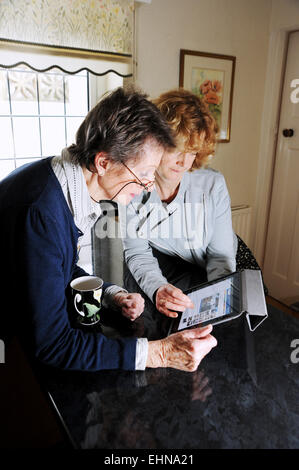 La vecchiaia pensionato femminile e più giovane donna utilizzando un iPad Apple tablet pc a casa Foto Stock