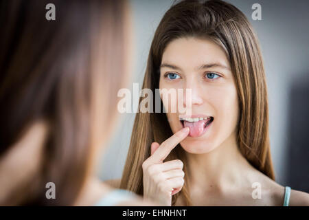 Donna esaminando la sua lingua in uno specchio. Foto Stock