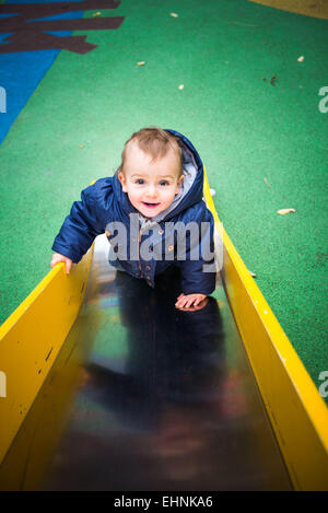 18 mese-vecchio baby boy su una diapositiva in un parco giochi. Foto Stock