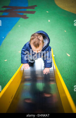 18 mese-vecchio baby boy su una diapositiva in un parco giochi. Foto Stock