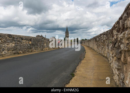 Road, Chiesa e passeggino su una strada nero in Saint-Emilion con cielo scuro e le nuvole. Foto Stock