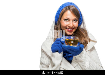 Moda giovane donna in una maglia blu inverno ensemble e cruscotto collo jersey sorseggiando una tazza di tè caldo con un sorriso in uno sforzo per mantenere in caldo, isolato su bianco Foto Stock