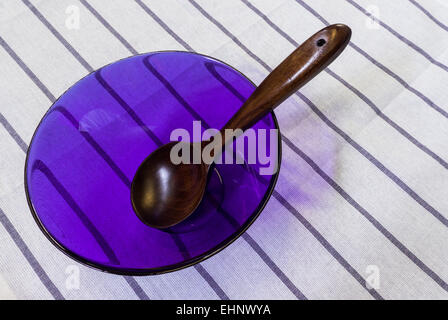 Cucchiaio di legno in luce viola la cottura di ciotola di vetro poste sul tavolo bianco sullo sfondo Foto Stock