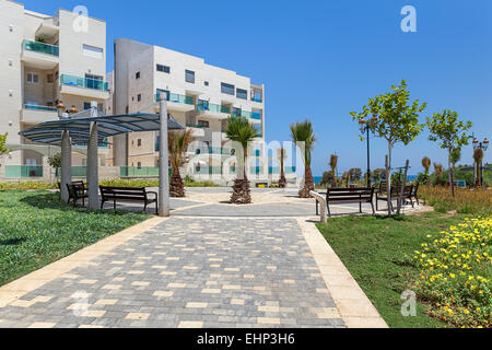 Città piccola piazza con palme e panchine vicino al complesso di moderni edifici residenziali in Ashqelon, Israele. Foto Stock