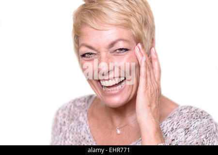 Close up felice Medioevo donna, con corti capelli biondi, ridere mentre si tocca il suo volto e guardando la telecamera. Foto Stock