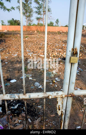 Aprire un campo disseminato di spazzatura e gusci di noce di cocco è visto attraverso un cancello chiuso con lucchetto in Skun, Kampong Cham Provincia, in Cambogia. Foto Stock