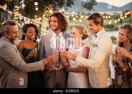 Coppia giovane e i loro ospiti con champagne flauti durante il ricevimento di nozze in giardino Foto Stock