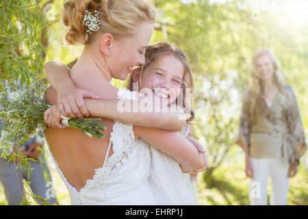 Sposa abbracciando damigella al ricevimento di nozze nel giardino interno Foto Stock