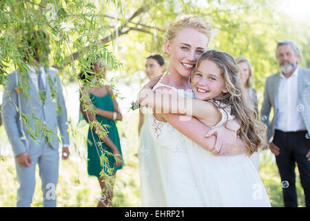 Sposa abbracciando damigella al ricevimento di nozze nel giardino interno Foto Stock