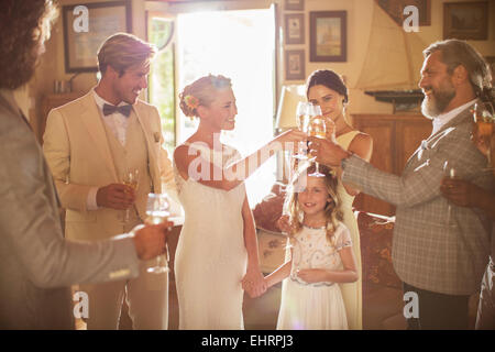 Coppia giovane e gli ospiti la tostatura con champagne durante il ricevimento di nozze in ambiente domestico Foto Stock