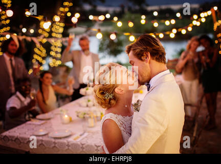 Coppia giovane baciare durante il ricevimento di nozze nel giardino interno Foto Stock