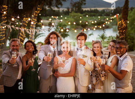 Ritratto di giovane coppia con gli ospiti la tostatura con champagne durante il ricevimento di nozze al crepuscolo Foto Stock