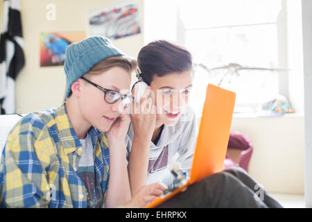 Due ragazzi adolescenti la condivisione di computer portatile e le cuffie in camera Foto Stock