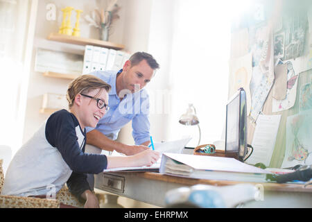 Padre aiutare nostro figlio adolescente che sta facendo il suo dovere in camera Foto Stock