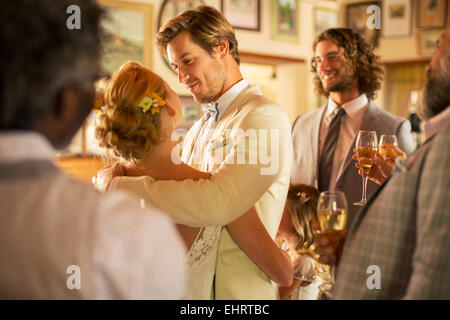 Sposo abbracciando sposa durante il ricevimento di nozze in ambiente domestico Foto Stock