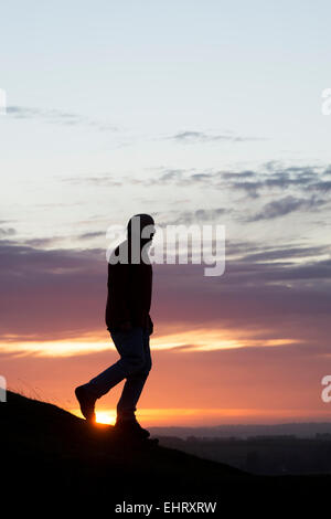 Uomo che cammina su una collina a sunrise. Silhouette. Regno Unito Foto Stock