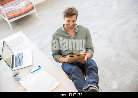 Ritratto di giovane uomo seduto con le gambe sulla scrivania in studio Foto Stock