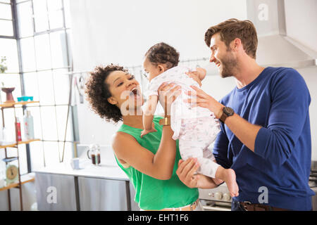 Genitori felici tenendo la loro bambina in cucina domestica Foto Stock