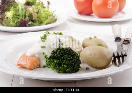 Filetto di salmone alla griglia con salsa al formaggio, patate di primizia e i broccoli, pomodoro e insalata fresca in background Foto Stock