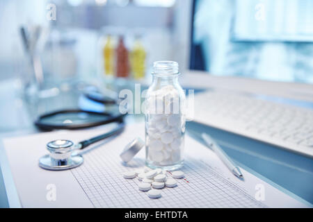 Pallone con le pillole di bianco, grafico e lo stetoscopio sulla scrivania Foto Stock