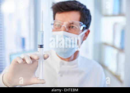 L'uomo nella mascherina chirurgica e labcoat tenendo la siringa di fluido Foto Stock