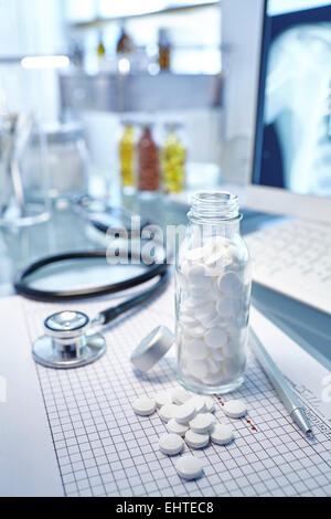 Pallone con le pillole di bianco, grafico e lo stetoscopio sulla scrivania Foto Stock