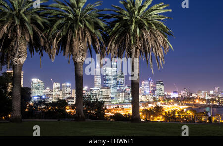 Lo skyline della città di Perth al tramonto, visto da King's Park con alberi di palma in primo piano. Foto Stock