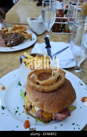 Anelli di cipolla fritti sulla grande gourmet hamburger di manzo extra con pancetta e formaggio bianco sulla piastra di cena Foto Stock