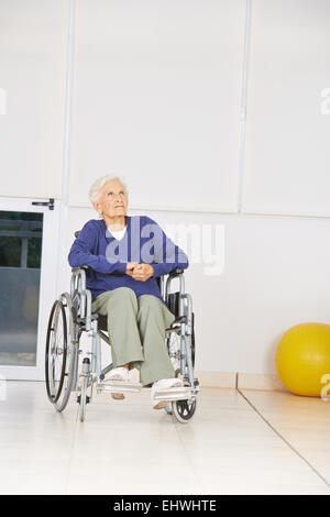 Vecchio pensieroso donna seduta in sedia a rotelle e guardando in alto in una casa di cura Foto Stock